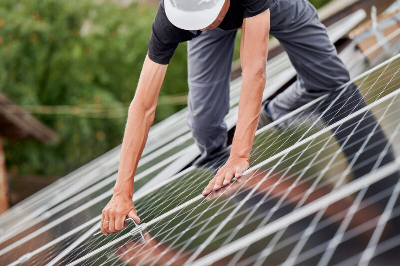 Man Installing Solar Panels On Energy Efficient Metal Roofing